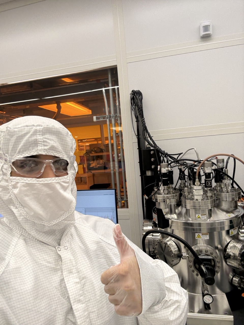 Sami in a cleanroom suit giving a thumbs up